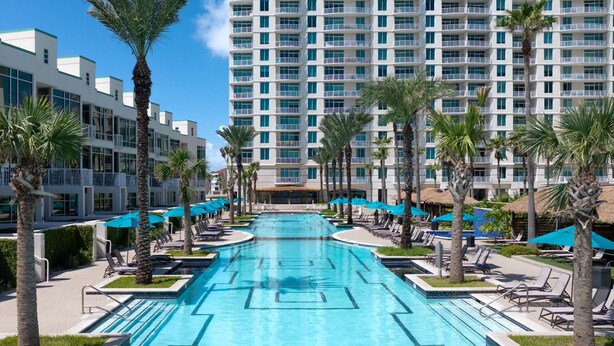 A swimming pool with lounge chairs and umbrellas, surrounded by palm trees and modern buildings. - Sapphire Condominiums 406 - 3 bedroom, 2 bath, ***All reservations require a 72 hour notice*** (South Padre Island)