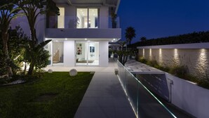 A modern two-story house with a glass facade, a balcony, and a well-lit entrance. - Luxury Sea View Villa with Pool in Santa Maria del Focallo – Villa Barbara, Sici (Ispica)