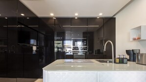 A modern kitchen with dark cabinetry, a central island with a sink, and a stainless steel faucet. - Luxury Sea View Villa with Pool in Santa Maria del Focallo – Villa Barbara, Sici (Ispica)