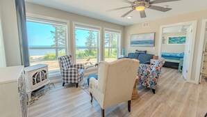 A spacious living room with a large window overlooking the ocean, a ceiling fan, and a fireplace.