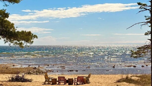 A beach with a row of wooden chairs and tables facing the ocean.