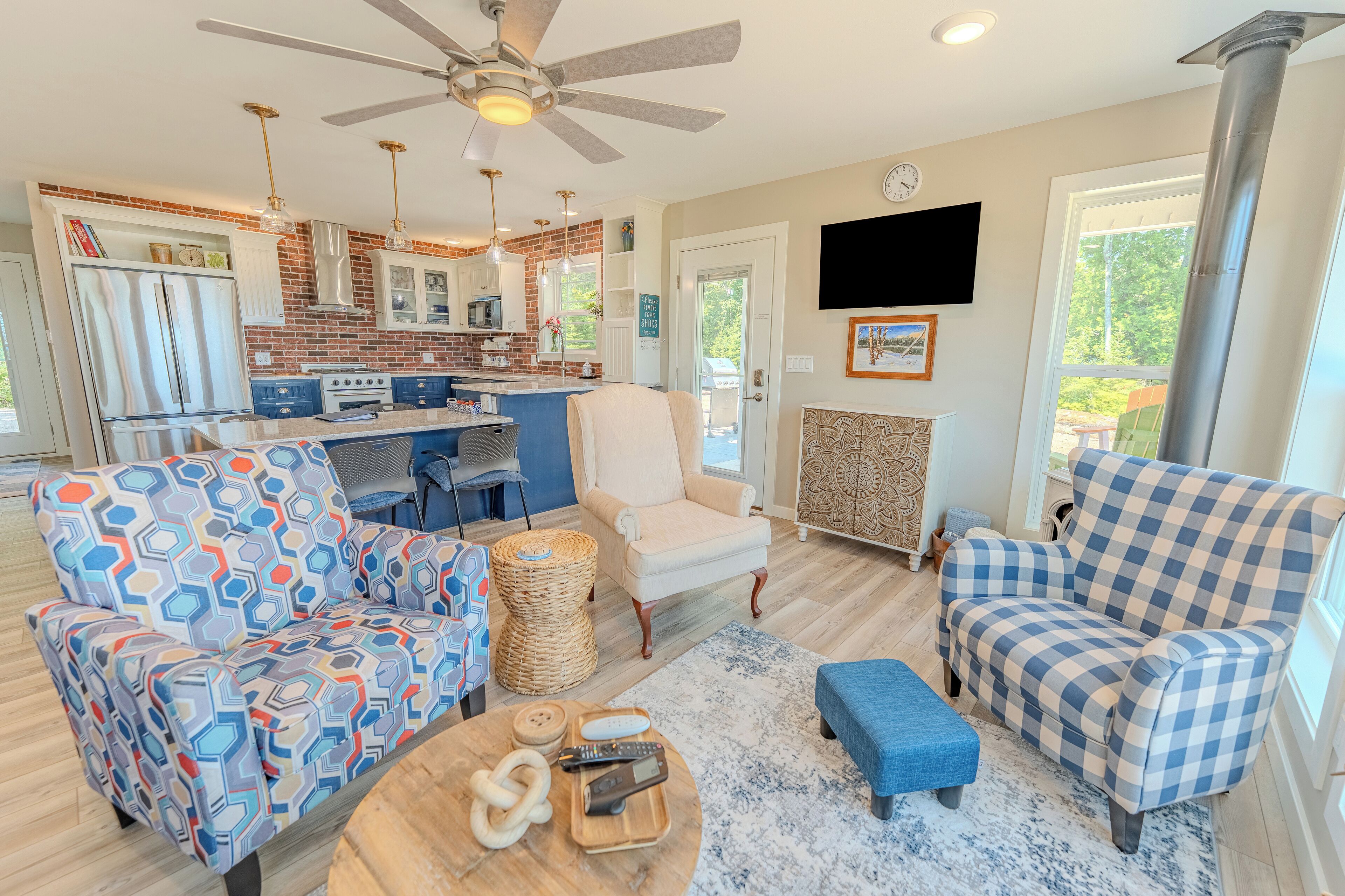 A modern kitchen with a central island, a dining area with a blue sofa and a patterned armchair, and a living room with a blue ottoman and a patterned rug.