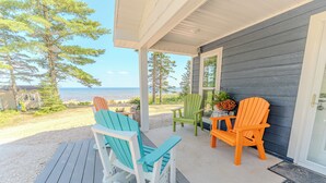 A covered porch with Adirondack chairs and a table, overlooking a beach and ocean.