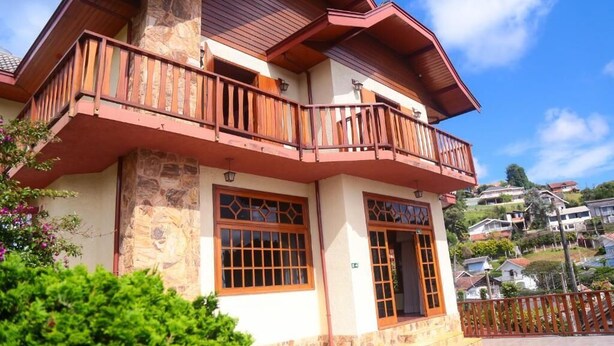 A two-story building with a stone facade, wooden balcony railings, and large windows with decorative glass panes. - Pousada DonaBella (Campos do Jordão)