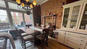Een eetgedeelte met een houten tafel en stoelen, een kroonluchter, een bakstenen muur en een keuken met witte kasten.