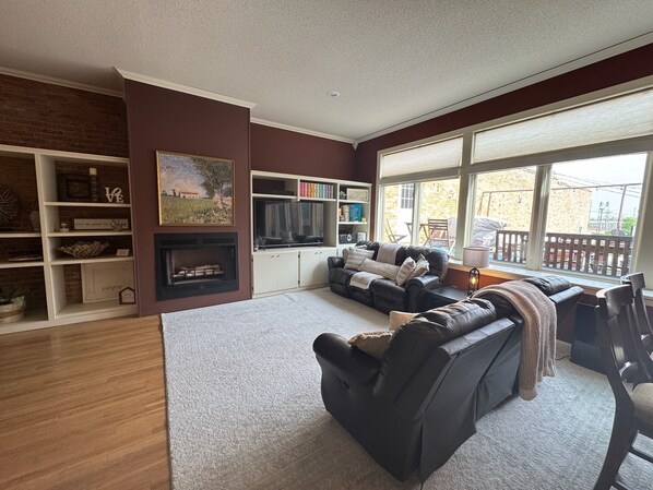 A living room with a fireplace, a sofa set, a bookshelf, and large windows. - Downtown Yankton loft, perfect to gather, unwind, and create lasting memories. (Yankton)