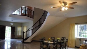 A spacious living area with a curved staircase, a dining table with chairs, and a ceiling fan. - exotic beach & villa with WiFi, AC in tranquil Tower Isle with pool (Tower Isle)