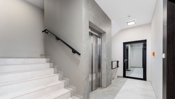 Ambiente moderno con una scala, un ascensore e un corridoio che porta a una porta.