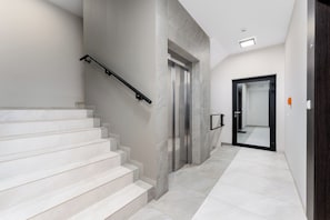 Ambiente moderno con una scala, un ascensore e un corridoio che porta a una porta.