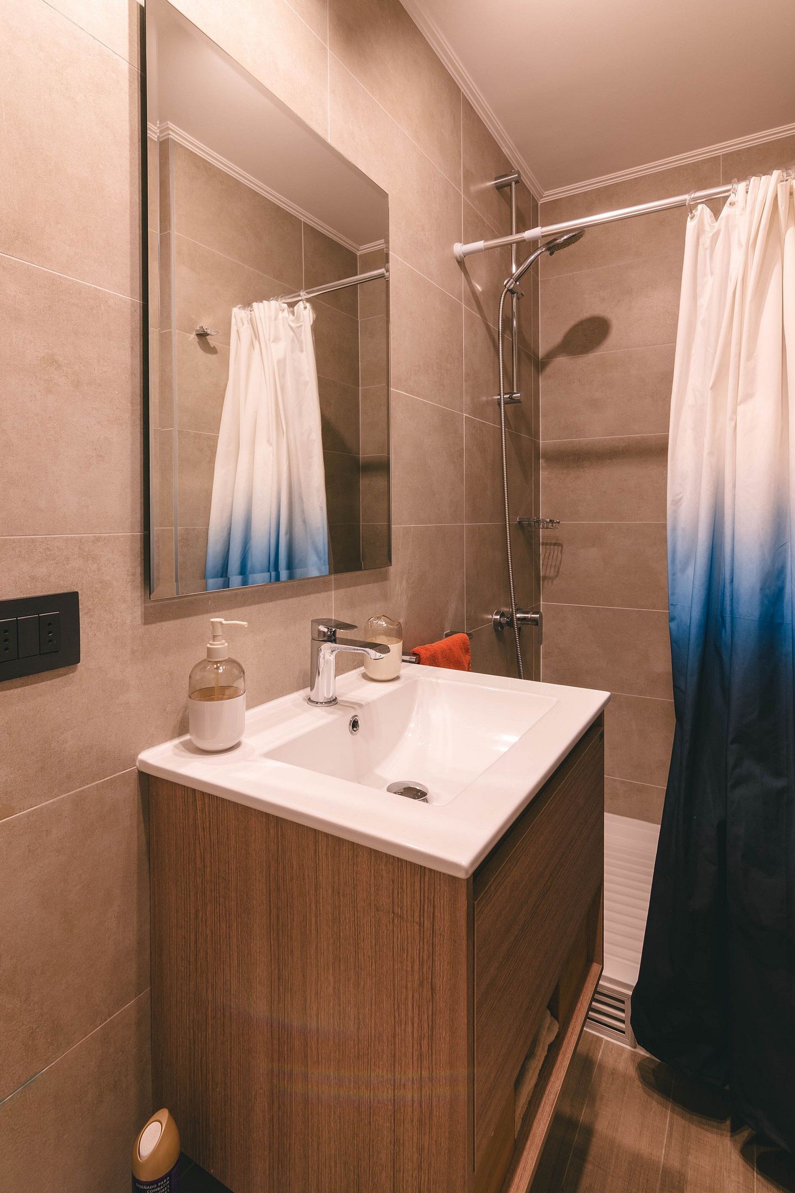 A modern bathroom with a large mirror, a white sink, and a shower area.