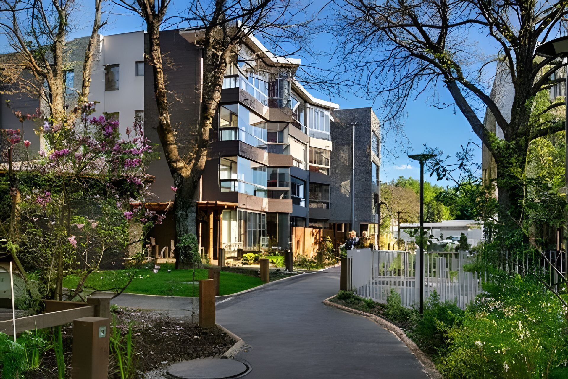 A modern residential building with multiple balconies, a paved driveway, and surrounding greenery.