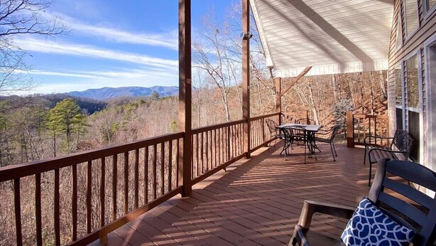 Une terrasse en bois avec une table et des chaises, offrant une vue sur un paysage montagneux.