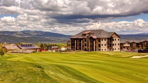 A large building with multiple floors, a well-maintained lawn, and a mountainous backdrop. - Steps to Cabriolet | Pool, Spa at Blackstone - Canyons Village Fun (Park City)