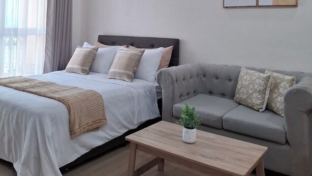 Una habitación de hotel moderna con una cama grande, un sofá gris, una mesa de centro de madera y dos obras de arte en la pared.