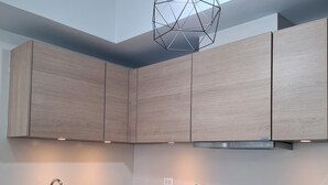 Una cocina moderna con armarios de madera, un lavamanos de acero inoxidable, una cafetera y una lámpara colgante geométrica única.