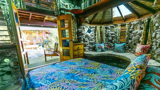 Una habitación con cama, pared de piedra, banco de madera y chimenea de piedra.
