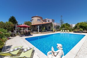 Una piscina con sillas de descanso, un edificio de piedra y una estatua.