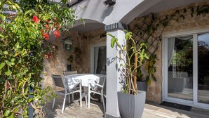 Un patio con un muro de piedra, una mesa y sillas blancas, y plantas en macetas.