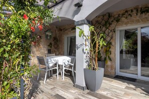 Une terrasse avec un mur en pierre, une table et des chaises blanches, et des plantes en pot.