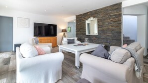 Una sala de estar moderna con una pared de acento de piedra, un televisor de pantalla plana y una mesa de comedor blanca.