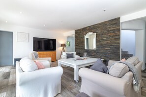 Un salon moderne avec un mur d’accent en pierre, un téléviseur à écran plat et une table à manger blanche.