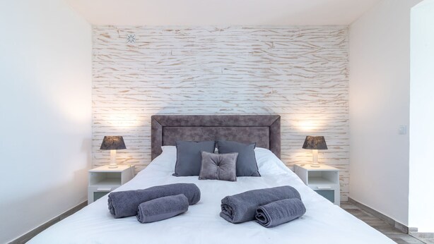 Una cama bien hecha con almohadas y toallas, dos lámparas de noche y una pared con textura.