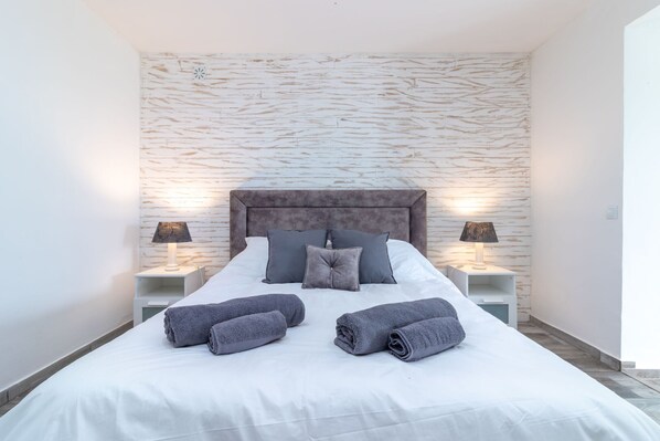 Un lit bien fait, avec des oreillers et des serviettes, deux lampes de chevet et un mur à motifs en arrière-plan.