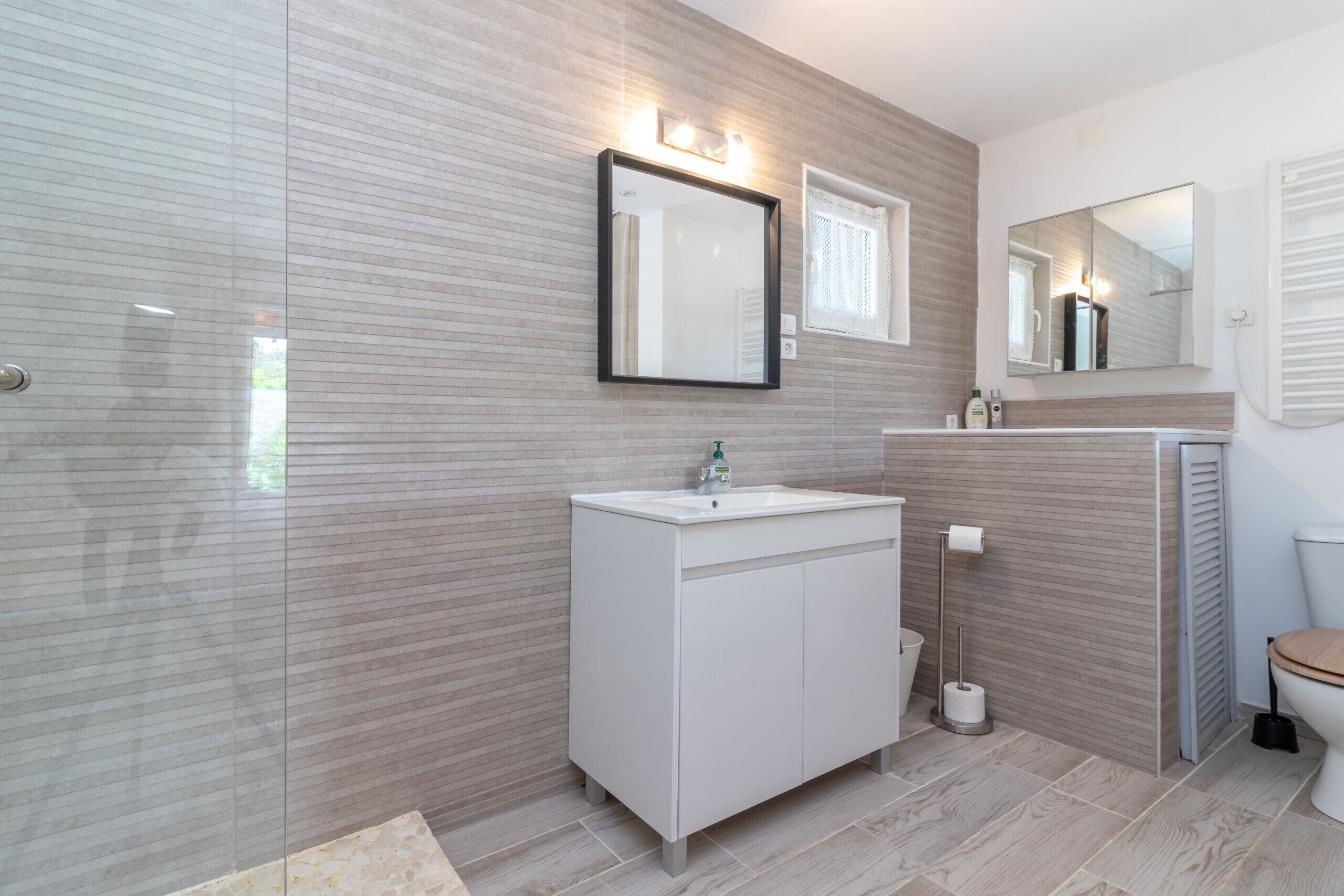 Un bany modern amb una dutxa envidrada, un lavabo blanc amb un mirall a sobre i un vàter amb seient de fusta.