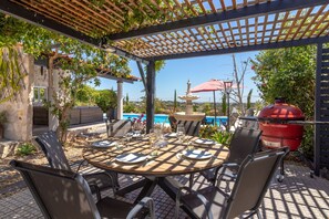 An outdoor patio with a round table set for dining, surrounded by chairs, under a wooden pergola with climbing plants. - Quinta Delsy - 5 Bed Villa With Pool Near Praia da Marinha (Lagoa)