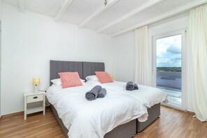 A double bed with two pillows, a nightstand with a lamp, and a view of the outdoors through a sliding door. - Quinta Delsy - 5 Bed Villa With Pool Near Praia da Marinha (Lagoa)