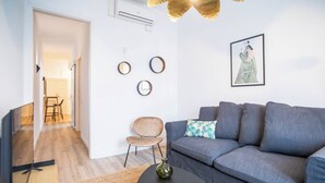 En moderne stue med en grå sofa, et lille rundt bord og en dekorativ vase. Vægure og et indrammet kunstværk hænger over sofaen.