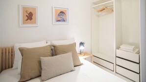 Et soveværelse med en seng, to puder, et natbord med en lampe, et klædeskab med et spejl, og to billeder hængende på væggen.
