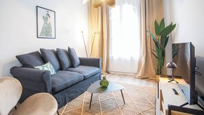 En moderne stue med en grå sofa, et lille sofabord, et fjernsyn og en stor plante.