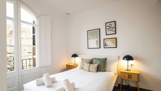 A neatly made bed with white linens and rolled towels, two bedside lamps, and two framed artworks on the wall.