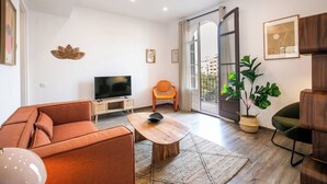 A modern living room with a sofa, a coffee table, a television, and a balcony with a view of buildings.