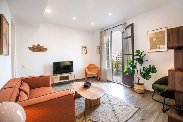 Una sala de estar moderna con un sofá, una mesa de centro, un televisor y un balcón con vistas a edificios.