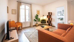 A living room with a sofa, chairs, a coffee table, a plant, and a bookshelf.