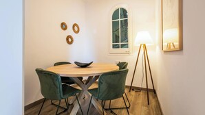 A dining area with a round table, four green chairs, a floor lamp, and a window with a view.