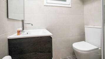 A bathroom with a white sink, dark wood vanity, white toilet, and a small window above the sink.