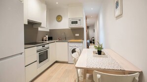 Eine kompakte Küche mit Mikrowelle, Backofen und Waschmaschine. Ein Esstisch mit Stühlen und ein kleiner Blumentopf sind ebenfalls vorhanden.