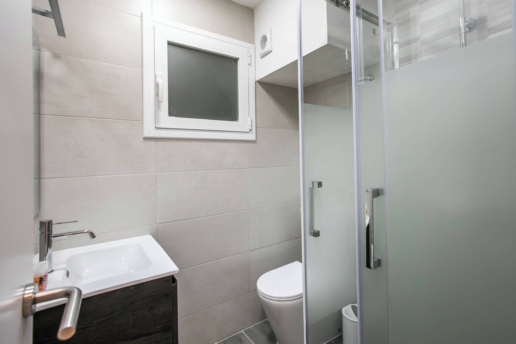 Een moderne badkamer met een douchecabine van glas, een wit wastafeltje en een toilet.