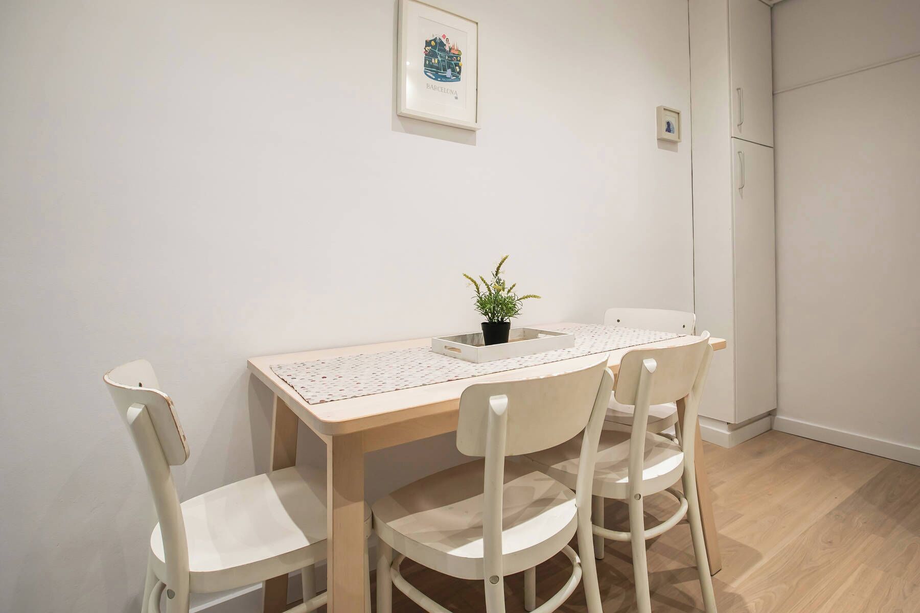 Een eethoek met een houten tafel en vier witte stoelen. Op tafel staat een kleine plant in een pot.