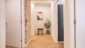 Un couloir avec un plancher en bois, un mur en briques et une petite table sur laquelle est posée une plante.