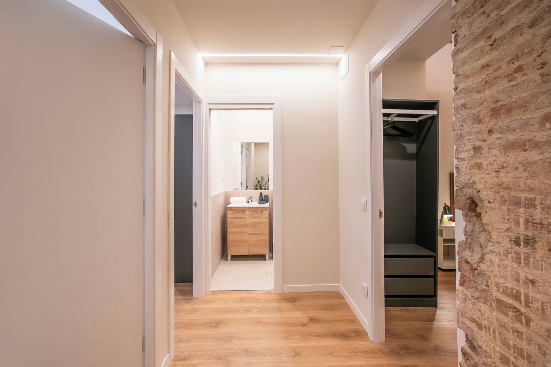 Een hal met houten vloer, een spiegel, een houten kast en een inloopkast met kledingroede.