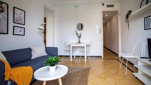 Uma sala de estar moderna com um sofá, uma mesa redonda pequena, um rack branco para TV e um espaço de jantar com uma mesa e cadeiras brancas.