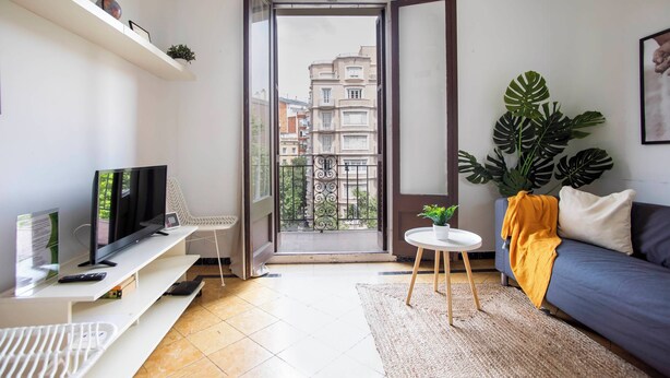 Uma sala de estar moderna com televisão, sofá e varanda com vista para edifícios.