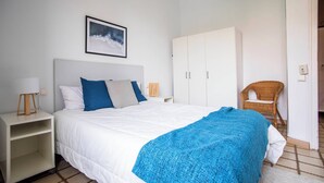 Quarto com cama, guarda-roupa branco e cadeira de vime.