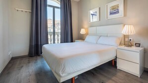 A hotel room with a large bed, bedside tables, a nightstand, a window with curtains, and two framed pictures on the wall.