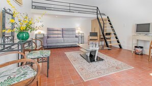 A living room with a sofa, chairs, a coffee table, a TV, a staircase, and a vase with flowers. - La Maison de Marius - SAINT BONNET DE JOUX (SAINT BONNET DE JOUX)