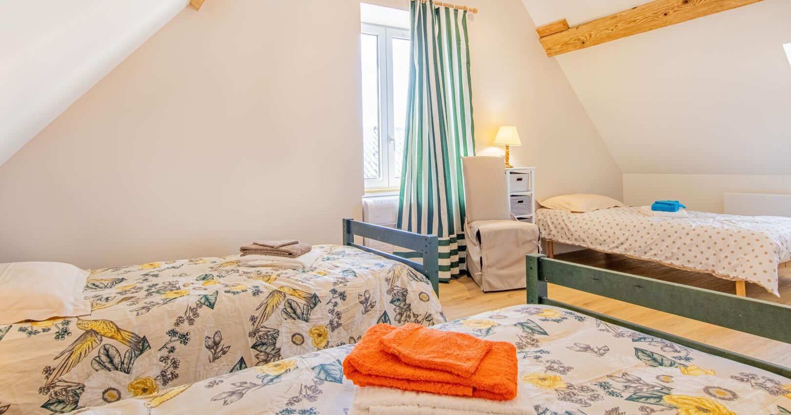 Une chambre confortable située sous les toits, avec deux lits, une fenêtre avec des rideaux, une lampe et un plafond en bois.